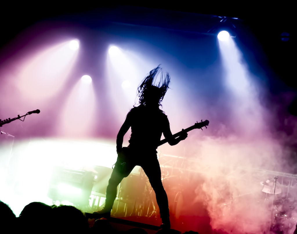 Silhouette of guitarist on stage with smoke and colored lights